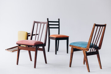 Four old wooden chairs with different colored seats stand empty on a white background, one chair inverted, selective focus