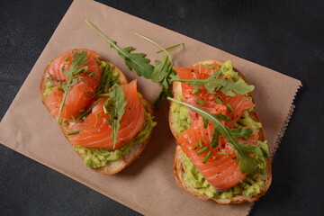 Whole grain bread with avocado paste and salmon, arugula leaves.