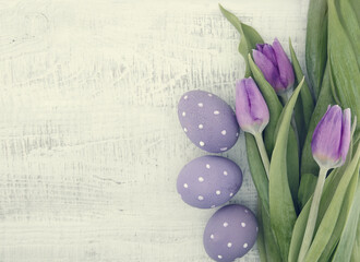 Bouquet of purple(violet) tulips and painted easter eggs on white rustic wooden background with copy space for message. Holiday greeting card. Top view. Flat lay