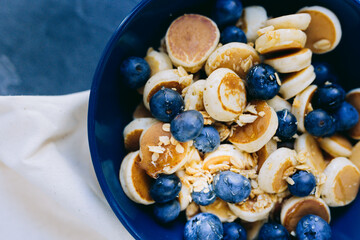 Close- up Mini Pancake cereal, mini pancakes in a dark blue bowl with sirup honey with blueberry