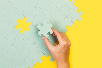 Mano sosteniendo una pieza de puzzle sobre un fondo de puzzle sobre un fondo amarillo. Vista...