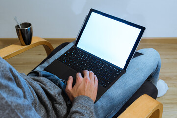 Young man holding laptop in lap, working on it, photographed from behind. black screen with coffee