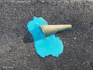 A waffle croissant with turquoise ice cream has fallen on the dark gray concrete floor and has become liquid and leaked. Close-up in two contrasting colors