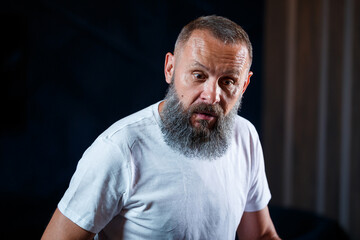 Emotional portrait of an adult gray-haired man with a beard in a white t-shirt