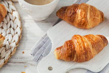 Delicious breakfast with fresh croissants and cup of coffee on a white wooden background. Delicious Baking