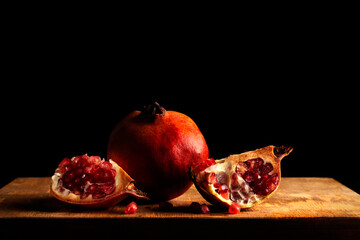 Still life with a whole pomegranate and two quarters on a wood and dark background in baroque style