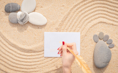 Fototapeta na wymiar Arrière-plan grains de sable de mer, sable fin de plage avec enveloppe et coquillages. Main féminine qui écrit sur une enveloppe. Emplacement pour texte sur papier. 