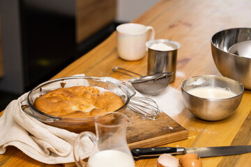 Tasty apple pie on a oaken wood table with a ingredients. Cooking a delicious apple pie on a kitchen in a loft style. Milk, eggs, sugar and a baked pie on a table. Home kitchen.