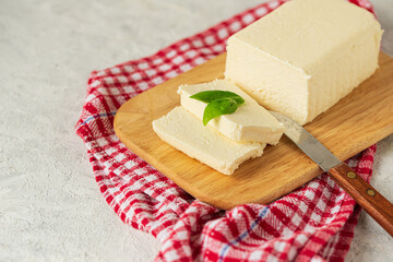 tofu, paneer, soy cheese, curd cheese, brynza, feta, Adyghe cheese with Basil and a knife on a wooden cutting Board on a light background