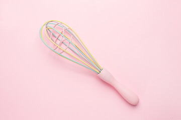 Multi-colored pastel kitchen whisk on pink background, cute kitchen utensils, feminine cooking