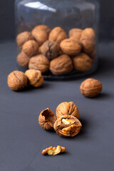 close-up peeled walnuts in shells on a black table and in a glass jar. brown nuts on a dark background. copy space. vertical. dried walnut and fruit. 