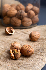 close-up three walnuts. unpeeled and peeled walnuts in shells on a black table and in a glass jar. brown nuts with sackcloth on a dark background. copy space. dried walnut and fruit. vertical