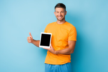 happy man in t-shirt holding digital tablet with blank screen and showing thumb up on blue