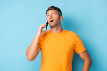 man in t-shirt talking on smartphone and looking up on blue