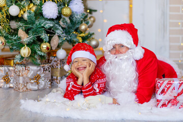 Santa Claus with a child near the Christmas tree hugging
