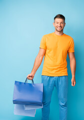 smiling man in t-shirt holding shopping bags on blue