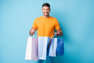 cheerful man in t-shirt holding shopping bags on blue