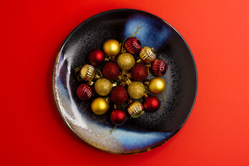Red and gold Christmas glass balls on a ceramic plate on a red background, topview.