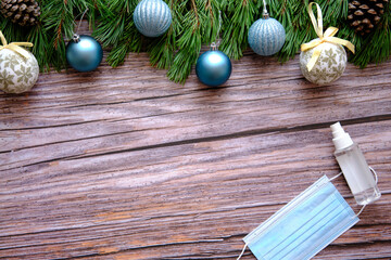 Obraz na płótnie Canvas Christmas composition with fir branches and white and blue baubles on wooden background. Medical mask and alcoholic gel