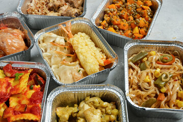 Takeout coronavirus food. Different aluminium lunch box with ravioli, curry chicken rice, gyoza tempura, noodles vegetables, lentils with pumpkin. covid-19 takeaway  food delivery.