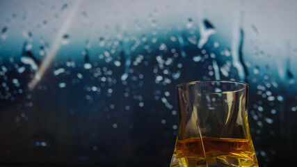 A glass of whiskey close-up, whiskey against the background of raindrops, a glass of whiskey on the...