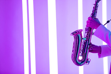 Fototapeta premium Male hands are holding a shiny saxophone against the background of neon lamps.