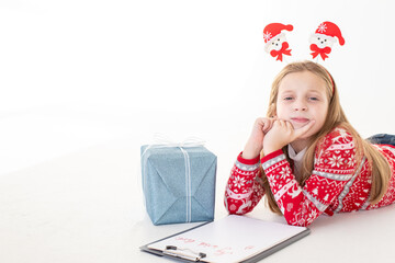 Thoughtful little girl writes letter to Santa Claus on white background.Goals plans dreams make to do list for new year christmas concept. Special orders for Santa. girl lying near the presents