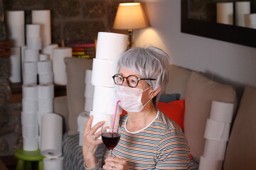 Senior woman hoarding lots of toilet paper drinking wine 