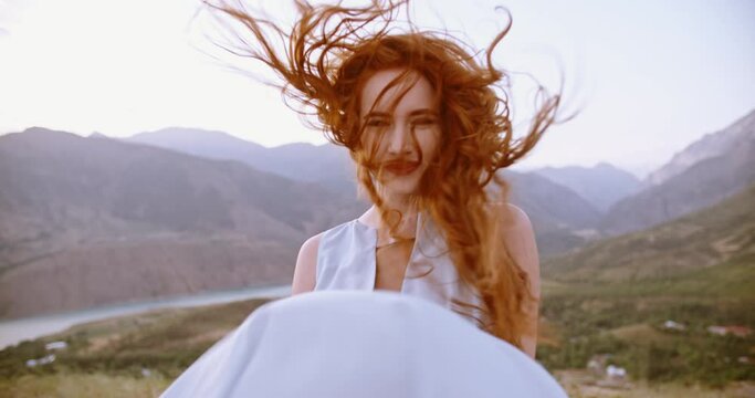 Beautiful caucasian girl wearing white dress on top of a mountain. Gorgeous woman looking at camera and positively smiling 4k footage