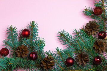 Postcard with a branch of blue spruce with cones and red Christmas balls on a pink background with place for text.