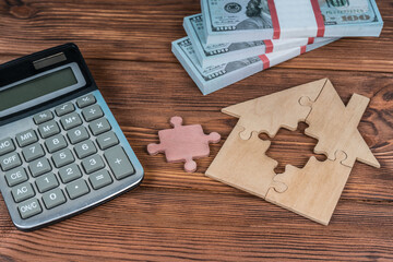 House of puzzle pieces, calculator and money bundles of dollar bills, on a wooden table. Concept idea, building a house, buying a sale. Realtor, loan, mortgage, court.