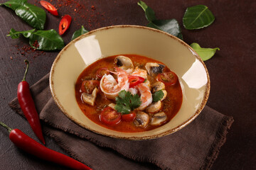 Thai cuisine. Tom yum. Coconut milk soup with shrimp, mushrooms, tomatoes, galangal root, lemongrass, chili pepper in a beige bowl on a brown table. Background image, copy space
