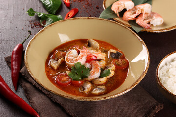 Thai cuisine. Tom yum. Coconut milk soup with shrimp, mushrooms, tomatoes, galangal root, lemongrass, chili pepper in a beige bowl on a brown table. Rice. Background image, copy space