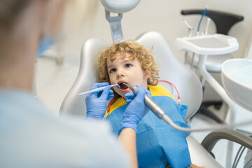 Cute young boy visiting dentist, having his teeth checked by female dentist in dental office.