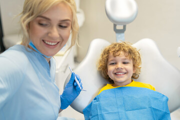 Cute young boy visiting dentist, having his teeth checked by female dentist in dental office.