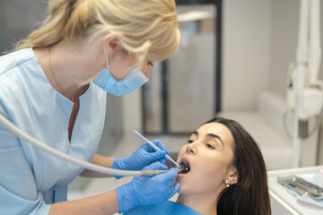 Fototapeta premium Female dentist in dental clinic providing examination and treatment of oral cavity for female patient.