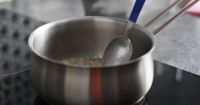 A female hand mixes milk porridge with a metal spoon in the kitchen. Morning diet breakfast