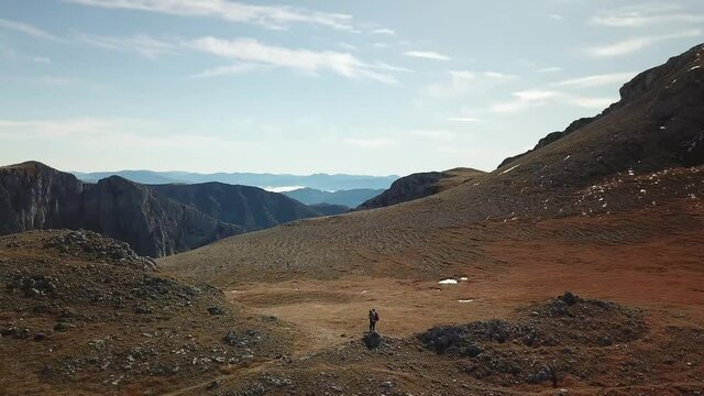 Drone shot of a couple walking to the peak of Fölzkogel in Hochschwab region, Austria. There are a few snow fields between the dried grass around them. Sunny spring day. Steep and sharp Alpine peaks. 