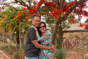 Happy mature couple embracing under a Red Formosa tree