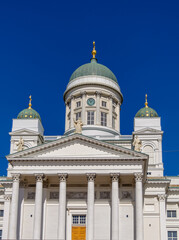 Fototapeta na wymiar Main entrance to white Helsinki Cathedral with neoclassical green dome with a clock, surrounded by smaller domes against bright blue sky.