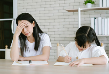 Upset Asian mother is angry to little daughter teach and doing homework writing and reading. Her...