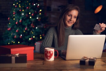 Woman using laptop, shopping online, using credit card at home. Christmas tree in the background.