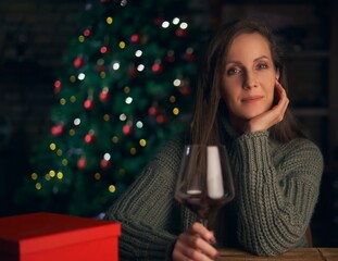 Portrait of beautiful woman toasting with red wine, smiling. Christmas tree in the background.