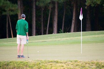 A man golfer viewing a golf ball on a golf green at a luxury hard and difficult country club golf course with woods or forest behind the male golfer.