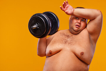 Fat man doing workout traning with dumbbells. Happy guy isolated over yellow background.