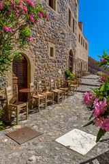 Fototapeta na wymiar Traditional cafe exterior in the fortified medieval castle of Monemvasia. Iron tables and wooden chairs with the view of the aegean sea in the background.