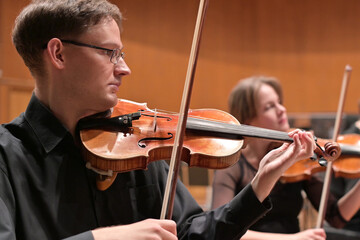 musicians in black clothes play violins rehearsing a performance