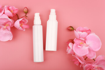 Flat lay with two unbranded creams in white bottles on pink background with flowers