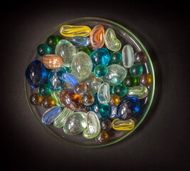 Glass colored decorative beads on a glass transparent saucer close up on a black background