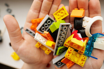 The child holds plastic construction blocks in his hands. Details in different and bright colors.